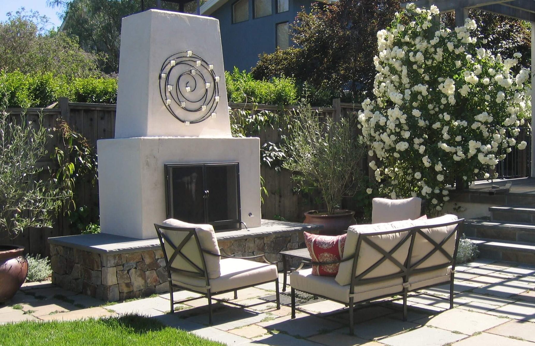 Outdoor fireplace and lounge seating on a stone terrace framed by flowering shrubs