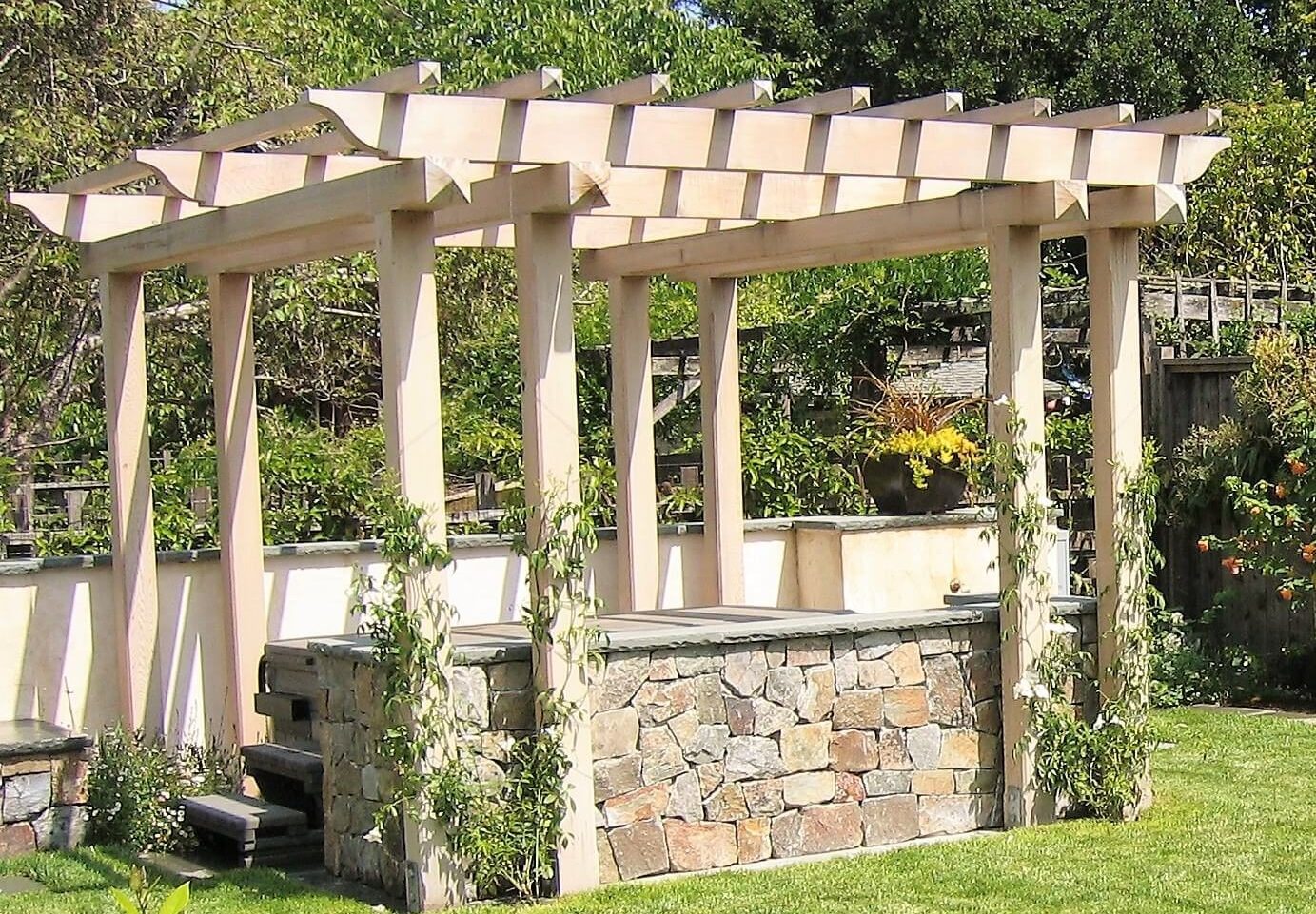 Stone-clad pergola over a spa with planting along the wall